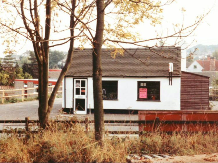 Small white building with a red-boarded shed, in autumn.