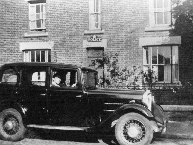 A motor car drawn up outside a house marked Police.