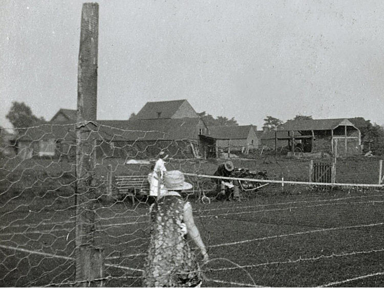 A man at work behind wire fencing, with buildings beyond.