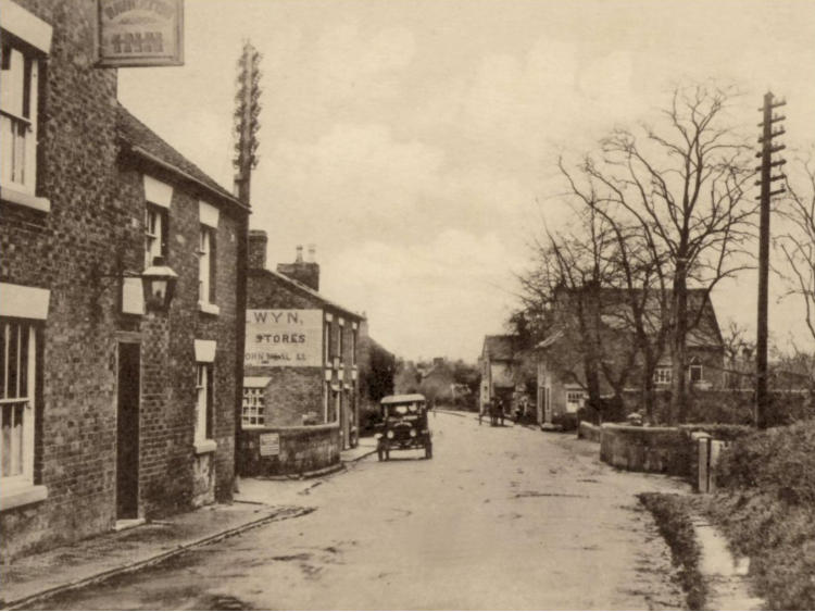 Street of buildings with a motor car and bare trees.